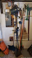 View of wall with hanging garden tools including watering can, rakes, snow shovels, hand pruner, and other tools clustered together