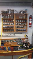 Wall-mounted wooden shelves filled with glass jars holding various nuts, bolts, screws, washers, and fasteners. A fire extinguisher is visible on the right.