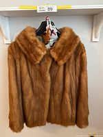 Front view of the handmade fox fur jacket hung on a hanger, showing the large collar and hook fastening.