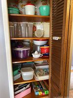 Full shelf view showing various Rubbermaid and Tupperware containers, bowls, pitchers, and wrap boxes in kitchen shelving with floral wallpaper.