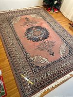 Full view of the large rose and blue patterned decorative rug on a hardwood floor with part of a Christmas tree visible.