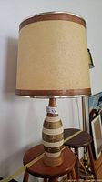 Full view of lamp showing beige fabric shade with wooden trim and chalkware base with sports figures.