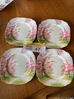 Four Royal Albert Blossom Time dessert plates with pink blossom tree designs laid out on wooden table showing full plate top views.