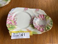 Two Royal Albert Blossom Time plates and a small ashtray displayed on a wooden table.
