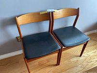 Front view of both teak dining chairs with black leather seats