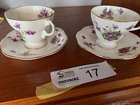 Two vintage Heathcote bone china cups and saucers displayed on wood surface with floral patterns and gold trim.
