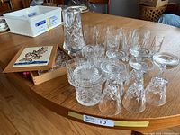 Wide view of the vintage crystal collection including glasses, vase, sugar bowl, sugar caddy, and napkin rings box on wooden table.