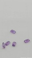 Five small, cushion cut deep purple amethyst gemstones arranged loosely on a neutral surface.