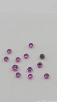 Close-up of 13 deep purple round cabochon garnet gemstones scattered on a white background.