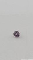 Close-up photo of the round cut purple pink sapphire showing color and cut details.