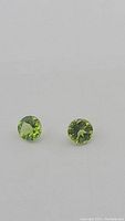 Close-up photo of two round apple green peridot gemstones, showing their cut and color details.