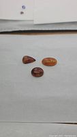 Three natural caramel amber cabochons of pear and oval shapes arranged on a flat surface with white background, displaying their smooth glossy finish and varied tones of warm amber color.