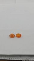 Pair of oval cut natural carnelian gemstones on plain background showing orange color with white streaks.