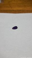 Close-up photo of a deep dark purple teardrop-shaped amethyst gemstone on white background, showing size and shape.