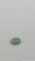 Front view of a smooth, polished oval cabochon natural green jade gemstone on white background.