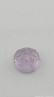 Close-up photo showing the hand carved floral pattern on the purple amethyst gemstone, revealing clarity and smooth surface details.