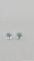 Close-up of the two round aquamarine gemstones showing diamond cut facets, light blue color, and size.