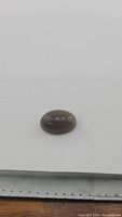 Oval cabochon moonstone placed on white background, showing smooth convex surface and warm smokey caramel color.