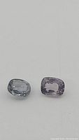 Close-up of two untreated purple spinels on a white background, showing their oval and cushion cuts and clarity.
