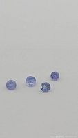Close up image showing four natural purple round cut tanzanite gemstones on light background.