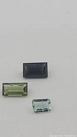Three rectangular tourmaline gemstones on white background showing color and cut.