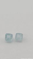 Close-up photo of two light blue square Sugarloaf cut aquamarine gemstones on a white background