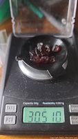 Several deep cherry red natural garnet crystals on a digital scale showing weight 30.51 carats