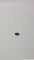 Photo of a single natural tanzanite gemstone showing oval cut and purple-blue color on flat surface.