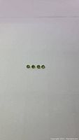 Four small round cut natural apple green peridot gemstones aligned horizontally on a white background.