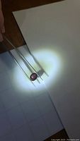 Oval cabochon star ruby gemstone held by tweezers under focused light showing size and shape.