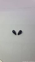 Pair of black polished tear drop shaped jade gemstones on white background. Internal holes visible for pendant use.