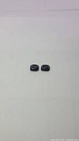 Top view of two cushion cabochon cut black jade gemstones placed side by side on white background showing smooth glossy surfaces and dark color.