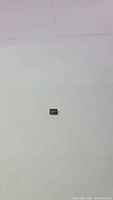 Clear view of a small rectangular emerald cut green tourmaline gemstone on white background.