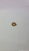 Pear cut natural golden citrine gemstone on a plain background showing the deep golden color and brilliance.