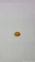 Photo of the honey jade cabochon gemstone on a plain background showing shape, color, and glossiness.