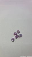Five natural lilac purple opal gemstones in cushion cabochon cut, scattered on white background.