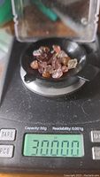 Photo showing raw multicolored tourmaline crystals on a black tray placed on a digital scale displaying 30.000 carats