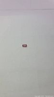 Photo of a single rectangular emerald cut padparadscha tourmaline gemstone on a white background, showing its deep pink color with orange tones.