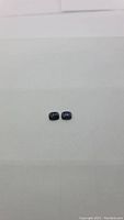 Two small deep purple cushion cab opal gemstones placed side by side on a plain white background, showing size and shape.