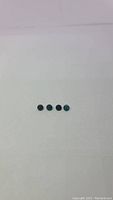 Four small round grandidierite gemstones laid in a row on a white background, diamond cut, showing deep bluish-green color.