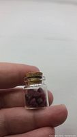 Glass vial held between fingers showing natural ruby crystals inside