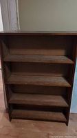 Front view of solid wood bookshelf showing four shelves with wood finish and wear.