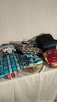 Full lot of boys clothing items arranged in four stacks showing a variety of shirts, pants, and pajamas mainly sizes 10-14.