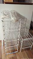 Photo showing stackable white wire shelving units with several sliding baskets, wire shelving panels, and accessories on wooden floor.