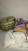 Photo showing green padded muscle suit, gray fabric cape with orange trim, white karate gi with Japanese characters