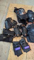 Mixed protective pads including elbow, knee, and wrist guards laid out on a floor showing wear and use