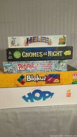 Stacked board games showing front titles: Melee, Gnomes at Night, Pictureka!, Blokus, Hop