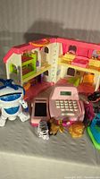 Front view of Little People house with pink toy cash register, small robot toy, and animal figures in front