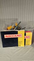 Vintage Meccano manuals with a plastic container of assorted metal parts in the background