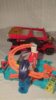 Red Hot Wheels semi-truck with detachable flatbed and orange-blue portable Hot Wheels track set with loops and ramps.